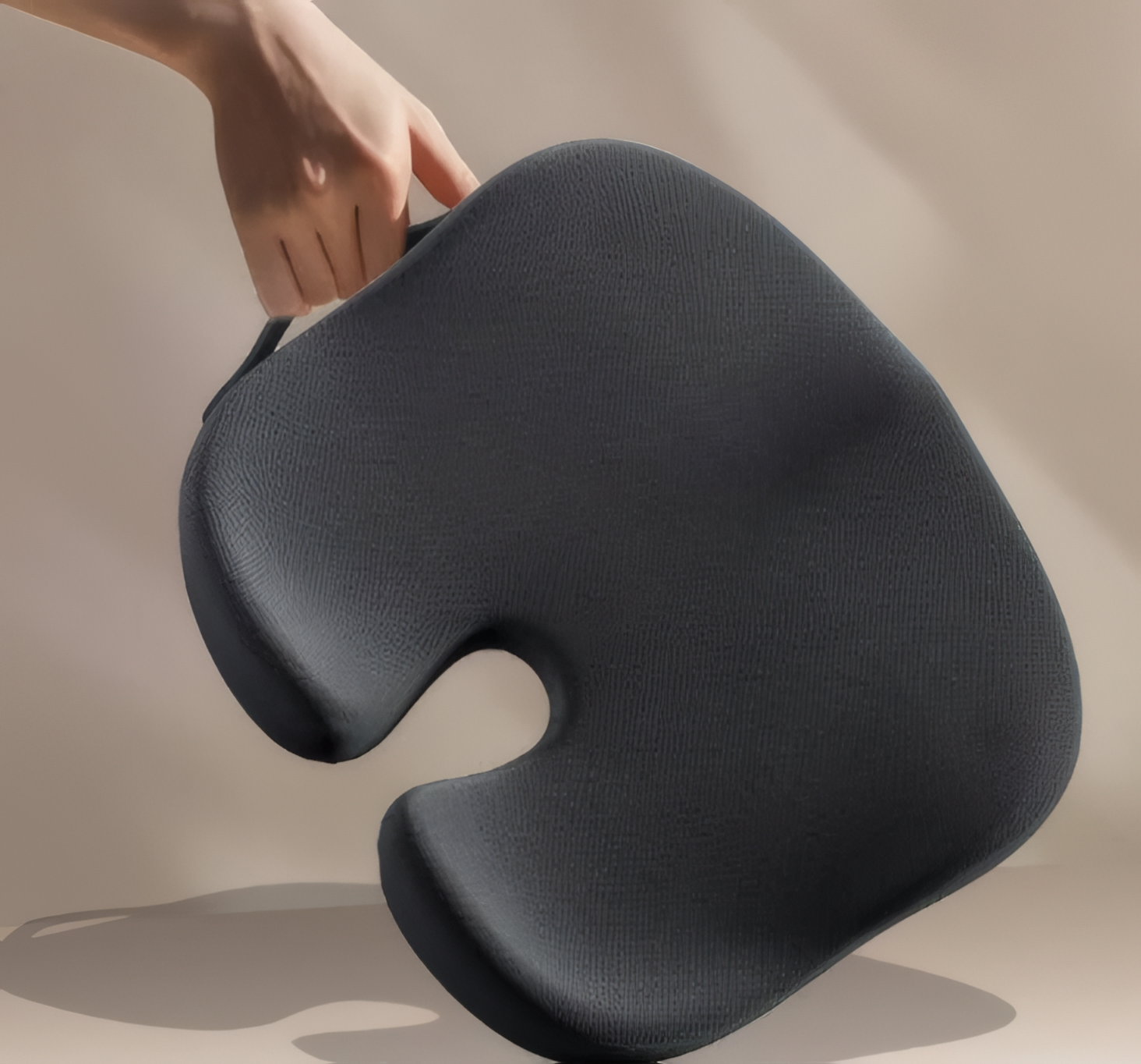 Person holding a dark gray U-shaped cushion against a beige background